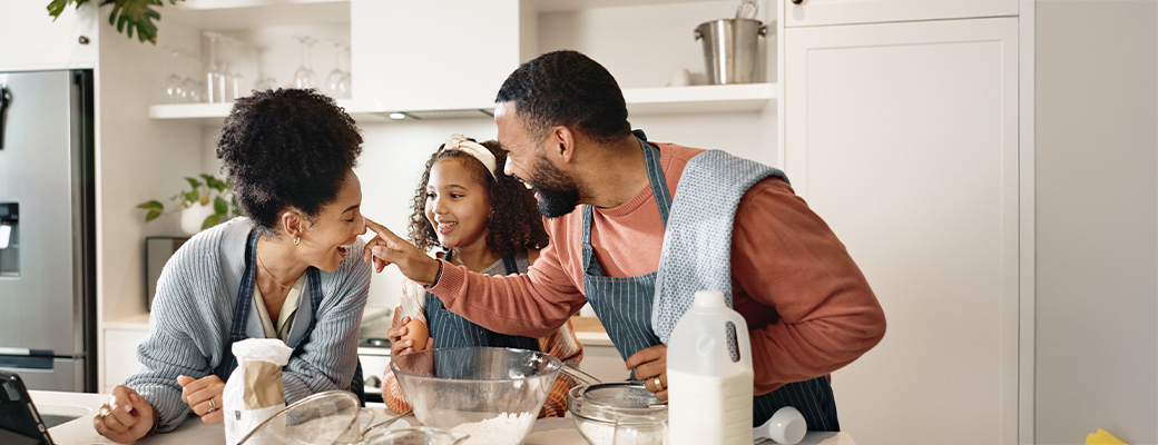 Image of couple and their young daughter in the kitchen and putting ingredients into a bowl 